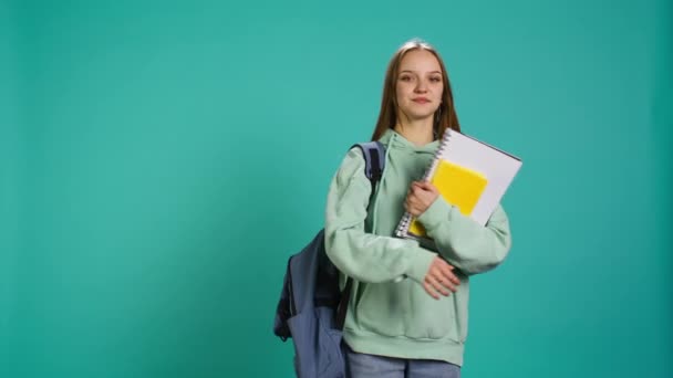 Egy vidám tinédzser portréja hátizsákkal, aki iskolai jegyzeteket és jegyzeteket tart, elszigetelve a stúdió hátterétől. Vidám diák iskolai felszereléssel a karjában, felkészülve az egyetemre, B kamera - Felvétel, videó