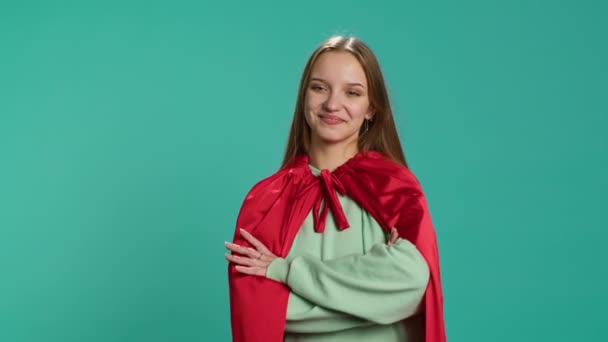 Сяюча жінка посміхається, зображуючи впевненого супергероя в червоному накидку, ізольованому на студійному фоні. Портрет веселого героїчного персонажа, який позує як потужний герой у костюмі, фотоапарат А - Кадри, відео