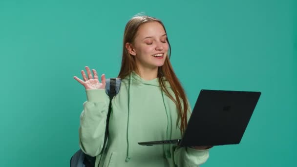 Mujer feliz saludando a los amigos durante la reunión de videoconferencia con el ordenador portátil, fondo del estudio. Chica saludando de la mano, compañeros de saludo durante el videocall de Internet en el portátil, cámara A - Metraje, vídeo