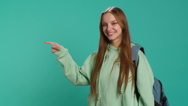 Radiant woman pointing finger towards empty space doing advertising, talking with audience. Smiling young girl doing presentation, showing copy text, studio backdrop, camera A - Séquence, vidéo