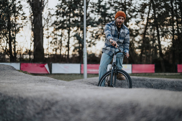 Un joven despreocupado con atuendo casual disfruta de un paseo en bicicleta en un parque pintoresco al atardecer. - Foto, imagen