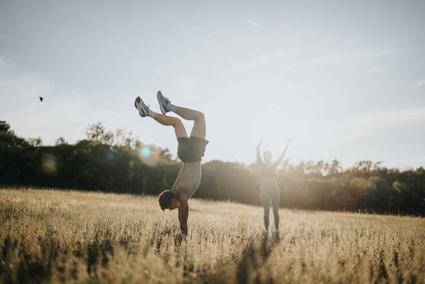 Deux personnes se livrant à des activités de fitness en plein air dans un champ serein sous la lumière du soleil. L'un effectue un handstand tandis que l'autre s'étire avec les bras levés. - Photo, image