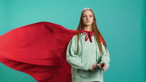 Šťastná mladá dívka zobrazující superhrdinu letící s pláštěm třepetajícím se ve větru, izolovaný přes studio pozadí. Portrét pozitivní hrdinky vydávající se za hrdinu v kostýmu, kamera B - Záběry, video