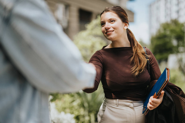 Uma jovem profissional em trajes inteligentes aperta a mão de uma pessoa invisível, transmitindo calor e simpatia em um ambiente urbano. - Foto, Imagem