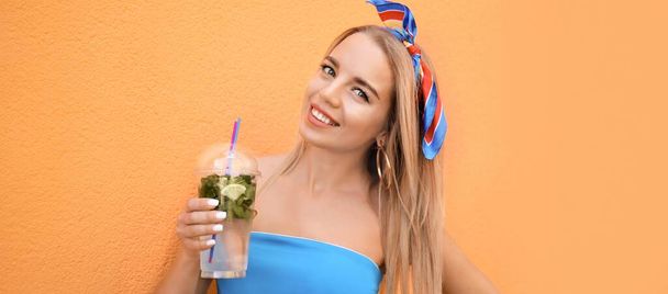 オレンジ色の背景に新鮮なカクテルをプラスチックカップで美しい若い女性 - 写真・画像