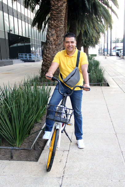 Der dunkelhäutige erwachsene Latino nutzt ein öffentliches Fahrrad, das er über eine App auf seinem Handy bezahlt, für nachhaltige Mobilität als Fortbewegungsmittel in der Stadt - Foto, Bild