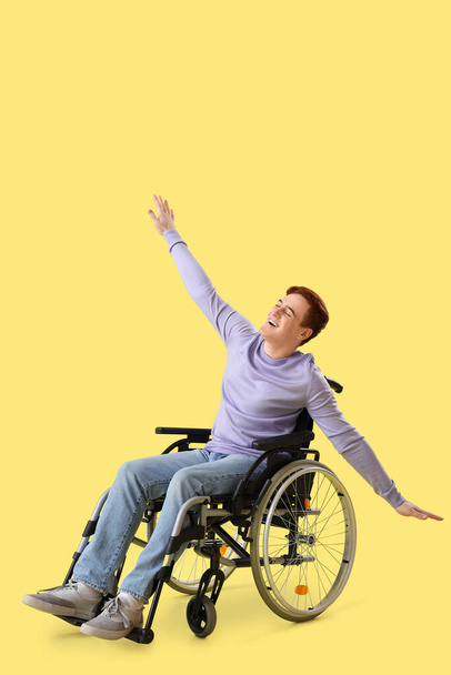 Szczęśliwy młody człowiek na wózku inwalidzkim na żółtym tle - Zdjęcie, obraz