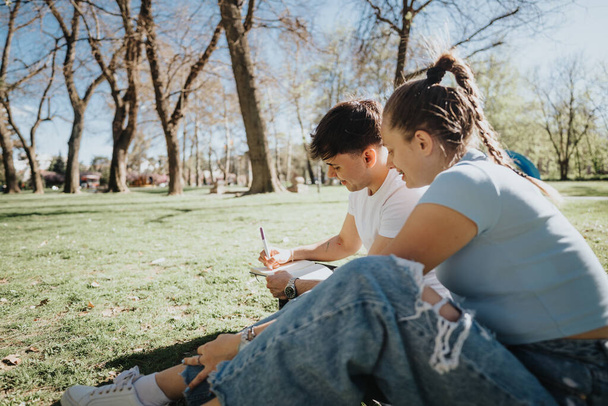 Dva středoškoláci spolupracují na domácím úkolu sedícím venku na trávě s atmosférou kampusu. - Fotografie, Obrázek