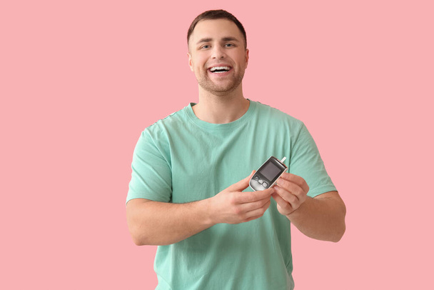 Όμορφος νεαρός ευτυχισμένος διαβητικός άνθρωπος με γλυκομετρικό σε ροζ φόντο - Φωτογραφία, εικόνα