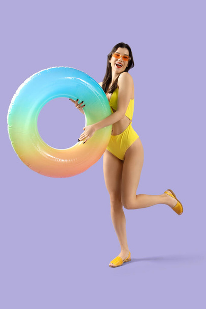 Beautiful young woman in beachwear with swim ring on lilac background - Photo, Image