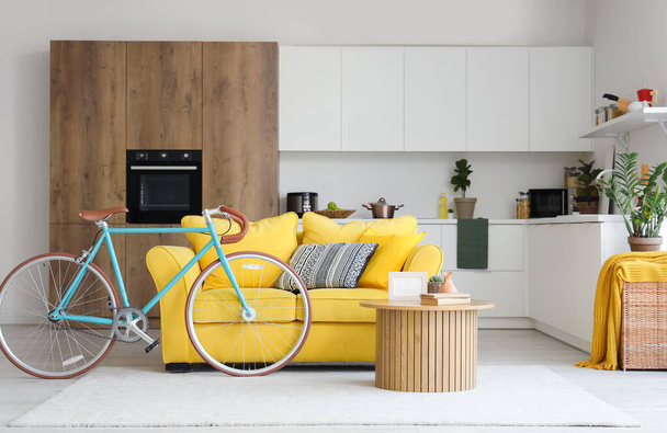 Εσωτερικό του όμορφου σαλονιού με κίτρινο καναπέ, τραπεζάκι σαλονιού, πάγκους και ποδήλατο - Φωτογραφία, εικόνα