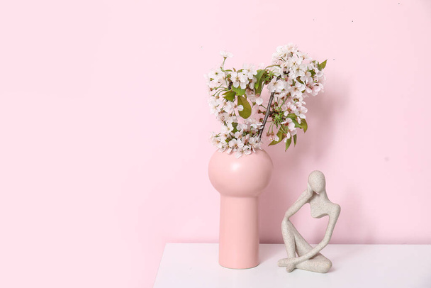 Vase with blossoming branches on table near pink wall in room - Photo, Image