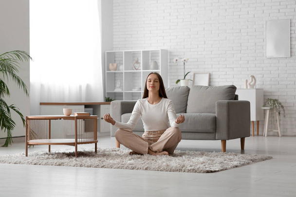 Молодая красивая женщина медитирует на полу рядом с диваном дома - Фото, изображение