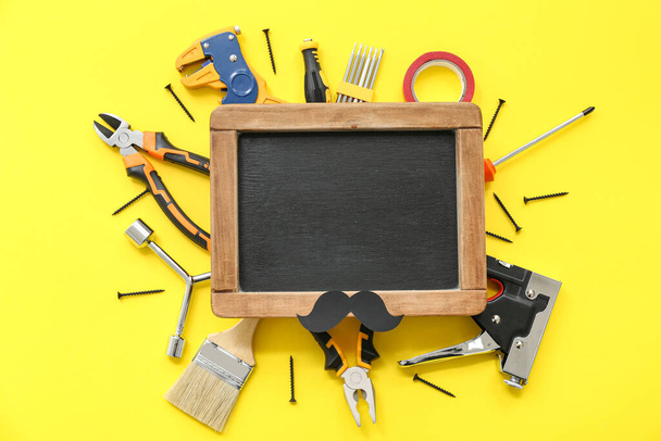 Tools, paper mustache and blank chalkboard on yellow background. Father's Day celebration - Photo, Image