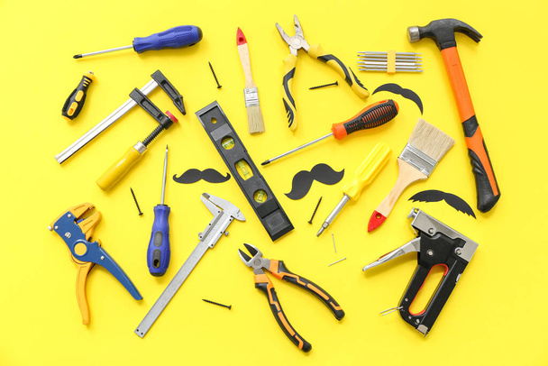 Werkzeuge und Schnurrbärte aus Papier auf gelbem Hintergrund. Vatertagsfeier - Foto, Bild