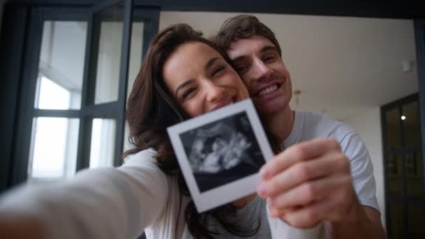 Кавказька сім'я посміхається щасливий сміх вагітна пара посміхається сміх жінка вагітність чоловік жінка чоловік дівчина обіймає поцілунки пудинг, показуючи ультразвукове зображення вдома збуджена дитина - Кадри, відео