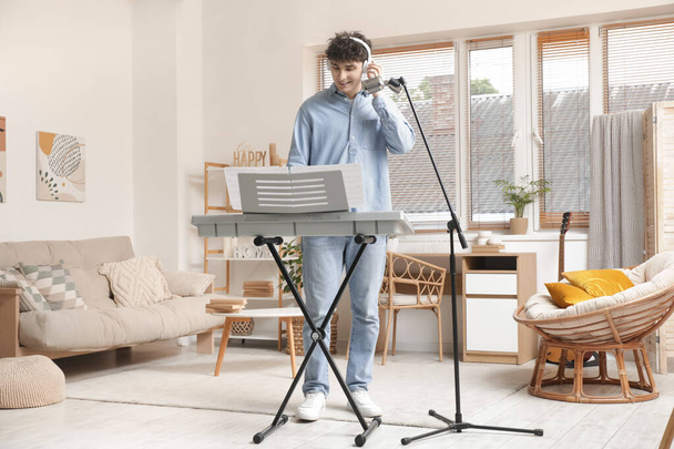 Joven guapo en auriculares con micrófono jugando sintetizador en casa - Foto, Imagen