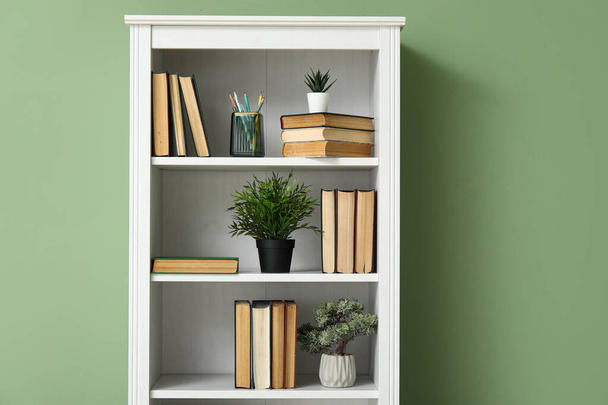Boekenkast met boeken en kamerplanten in de buurt van groene muur in de kamer, close-up - Foto, afbeelding