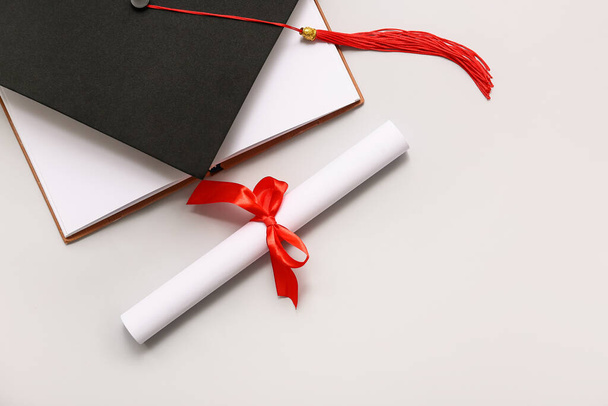 Δίπλωμα με κόκκινη κορδέλα, ανοιχτό βιβλίο και καπέλο αποφοίτησης σε λευκό φόντο - Φωτογραφία, εικόνα