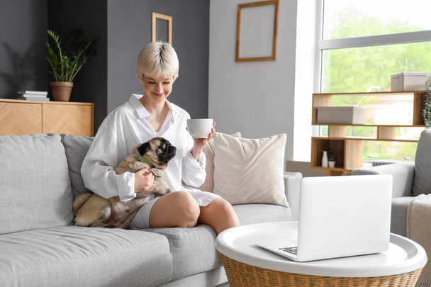 Mladá žena s šálkem kávy a pug dog sedí na pohovce doma - Fotografie, Obrázek