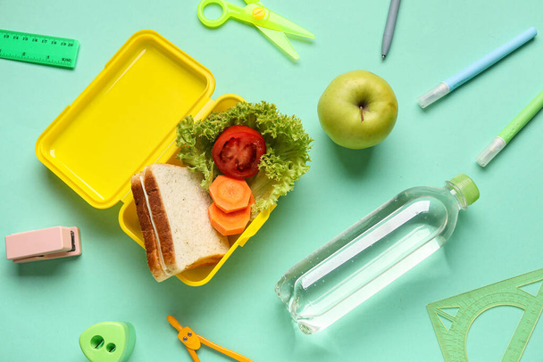 Almuerzo con sabrosa comida, botella de agua y papelería sobre fondo de color - Foto, Imagen