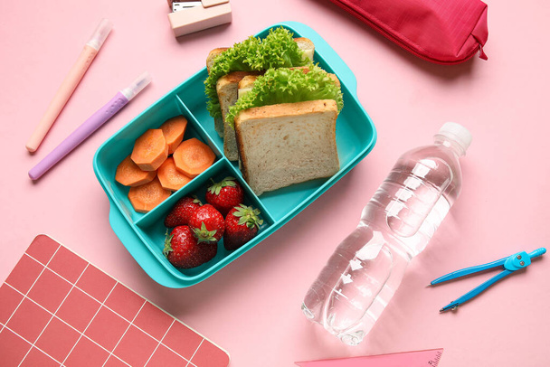 Γεύμα με νόστιμο φαγητό, μπουκάλι νερό και γραφική ύλη σε ροζ φόντο - Φωτογραφία, εικόνα