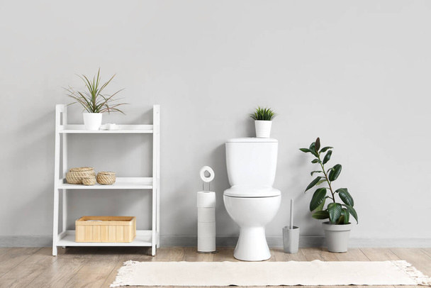 Innere Toilette mit Toilettenschüssel, Regal und Pflanze in der Nähe der grauen Wand - Foto, Bild