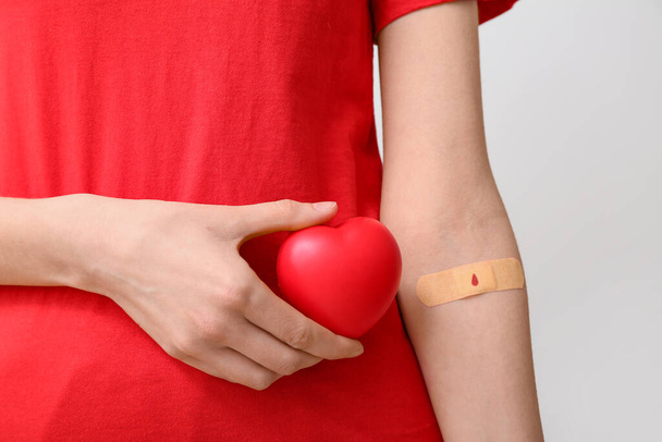 Γυναίκα με σχήμα καρδιάς λαβή μπάλα και εφαρμόζεται ιατρικό έμπλαστρο σε γκρι φόντο. Παγκόσμια Ημέρα αιμοδοσίας - Φωτογραφία, εικόνα