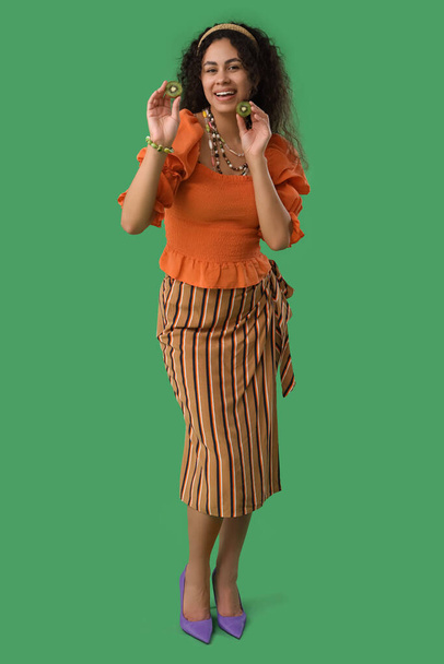 Hermosa joven feliz mujer afroamericana con rodajas de kiwi sobre fondo verde - Foto, Imagen
