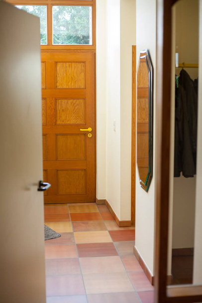 Cozy entrance hallway with wooden front door, tile flooring, decorative mirror, creating warm atmosphere - Photo, Image