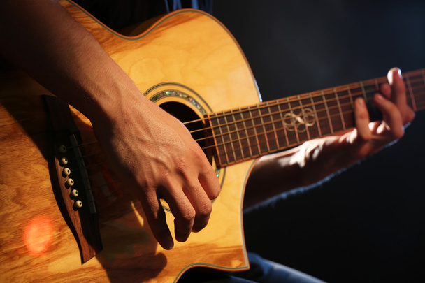 Young man playing on acoustic guitar on dark background - Photo, Image