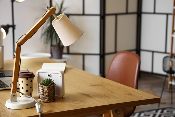 Schreibtischlampe, Zimmerpflanze und Tasse zum Mitnehmen auf Holztisch im Büro, Nahaufnahme - Foto, Bild