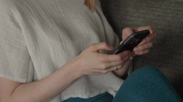 Lähikuva nainen käyttää älypuhelinta istuessaan sohvalla. Keskity käsiin ja laitteeseen. - Materiaali, video
