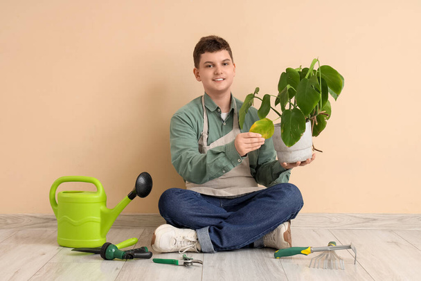 Jardinier adolescent avec plantes et outils assis près du mur beige - Photo, image