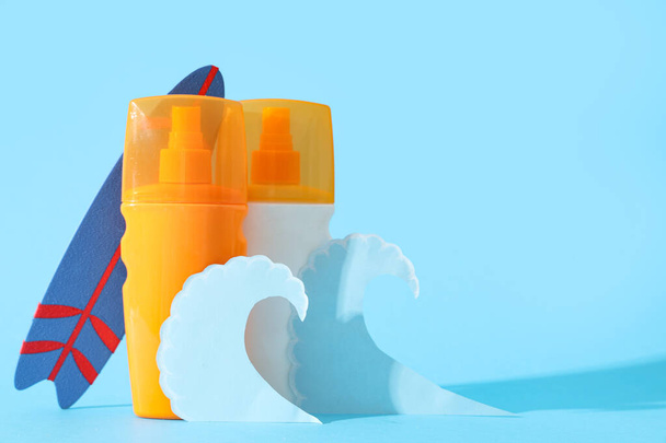 Состав с бутылками крема от загара, мини-серфинга и бумажных волн на цветном фоне - Фото, изображение