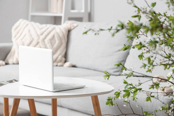 Gemütliche Couch, Couchtisch, Laptop und blühende Zweige im Wohnzimmer - Foto, Bild