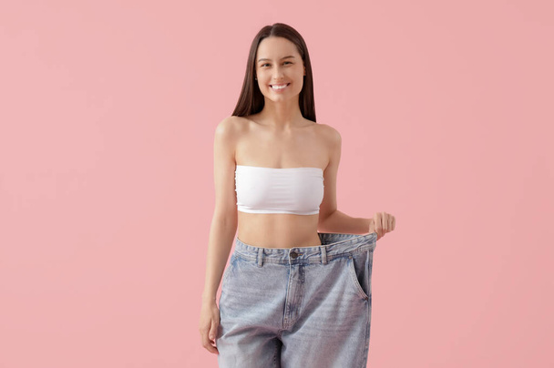 ピンクの背景に緩いジーンズで美しい若い幸せな女性. 減量コンセプト - 写真・画像