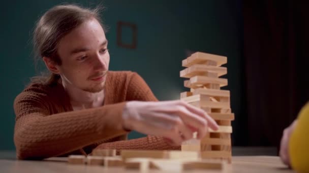 Un uomo che gioca a giochi da tavolo a casa, impilando e rimuovendo i blocchi di legno con precisione in un ambiente casual. Copia spazio - Filmati, video