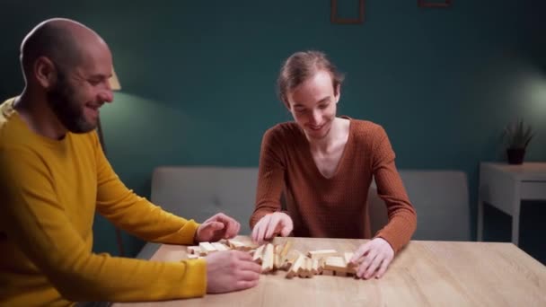 Two men are having a good time playing a game of wooden blocks building tower at home, creating a comfortable and enjoyable indoor ambiance. Copy space - Footage, Video