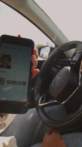 Primer plano vertical de la mano de una mujer irreconocible sentada en un automóvil sosteniendo un smartphone y demostrando una licencia de conducir digital - Imágenes, Vídeo