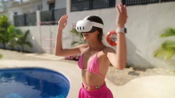 Pembe bikinili genç bir kadın yüzme havuzu kenarında sanal gerçeklik deneyiminin tadını çıkarıyor, eğlenceli anları yakalıyor.. - Video, Çekim