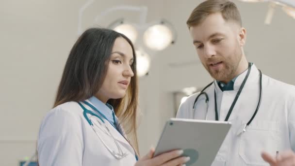 Kaksi lääkäriä, jotka tarkistavat potilaan tiedot tabletista - Materiaali, video