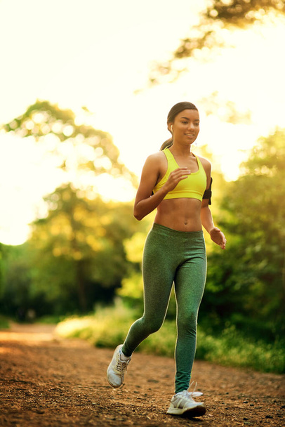 Kültéri, nő és fut a fitness, a testmozgás és a kardio rutin sport mosollyal. Természet, női futófelület és fülhallgató maratoni állóképességgel, edzéssel és wellness célú ellenálló képességgel. - Fotó, kép