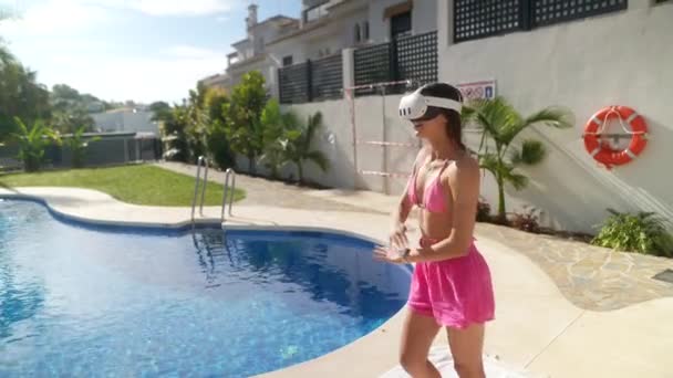 Une femme s'amuse au bord d'une piscine par une journée ensoleillée, portant un casque VR pour une expérience de réalité virtuelle - Séquence, vidéo