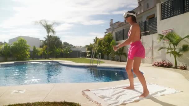 Μια γυναίκα διασκεδάζει με ένα παιχνίδι VR δίπλα στην πισίνα μια ηλιόλουστη μέρα, απολαμβάνοντας μια σύγχρονη δραστηριότητα αναψυχής σε εξωτερικούς χώρους - Πλάνα, βίντεο