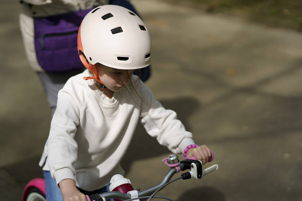 スプリングパークを通ってヘルメットに乗る小さなかわいいサドガールサイクリスト - 写真・画像