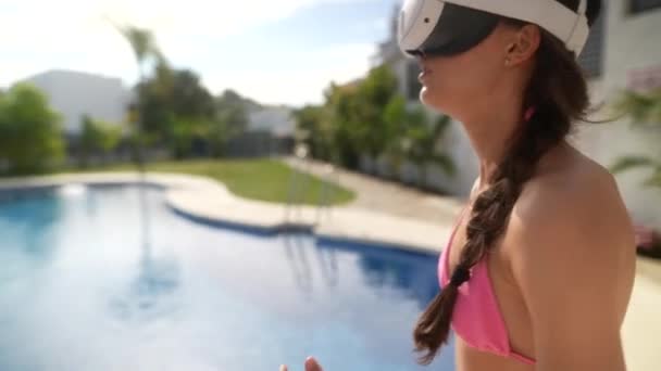 Frau im Badeanzug mit VR-Headset am Pool genießt Sommerfreizeit mit Virtual-Reality-Erfahrung. - Filmmaterial, Video