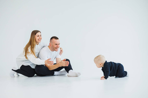 Молодая счастливая семейная пара с маленьким сыном на белом фоне. Мама и папа с ребенком на белом фоне. - Фото, изображение
