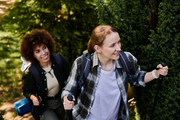 Una joven pareja de lesbianas sonríe mientras caminan juntos por un frondoso bosque verde. - Foto, Imagen