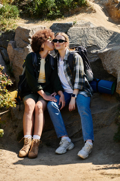 Una giovane coppia lesbica si gode un'escursione nella natura selvaggia, condividendo un momento tenero su uno sperone roccioso. - Foto, immagini